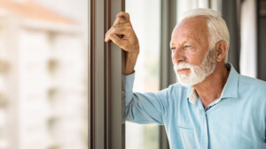 Serious senior man looking through window of his apartment.