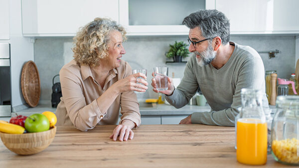 Cheerful mature couple drinking water and relaxing in the kitchen at home